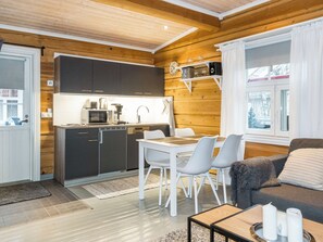A compact kitchen with modern appliances, a dining area with white chairs, and a cozy seating area with a sofa. - Renkitupa by Interhome (Rovaniemi)