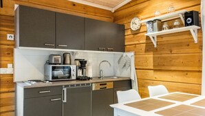 Una cocina compacta con microondas, cafetera y lavamanos. Se observa una mesa blanca con un mantel individual y dos sillas.