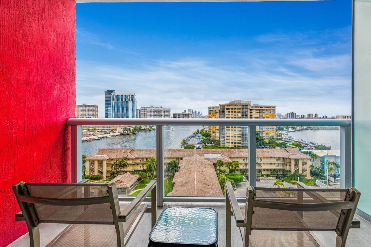 Un balcón con dos sillas y una mesita, con vistas a un puerto deportivo y al paisaje urbano.