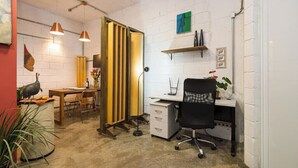 Ein moderner Arbeitsraum mit weißer Ziegelwand, Holztisch, schwarzem Bürostuhl und gelbem Vorhang.