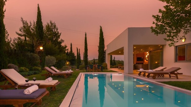 Un espace piscine extérieur moderne, doté de chaises longues et d’un espace intérieur bien éclairé.