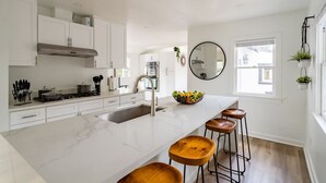 Een moderne keuken met witte kasten, een groot kookeiland met krukken, een roestvrijstalen afzuigkap en een grote spiegel boven de gootsteen.
