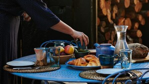 Una mesa de desayuno con croissants, frutas y una jarrón.