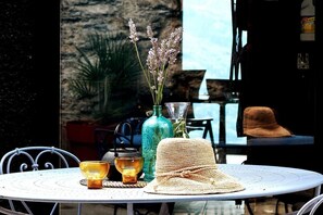 A round table with a woven hat, a glass vase with flowers, and two candle holders.