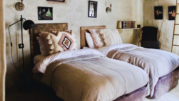 A bedroom with a wooden headboard, two beds with white bedding, a floor lamp, and a bookshelf with books.