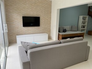 Uma sala de estar moderna com um sofá cinzento, uma TV de tela plana fixada numa parede de tijolos, um móvel de entretenimento branco e uma mesa de centro de madeira.