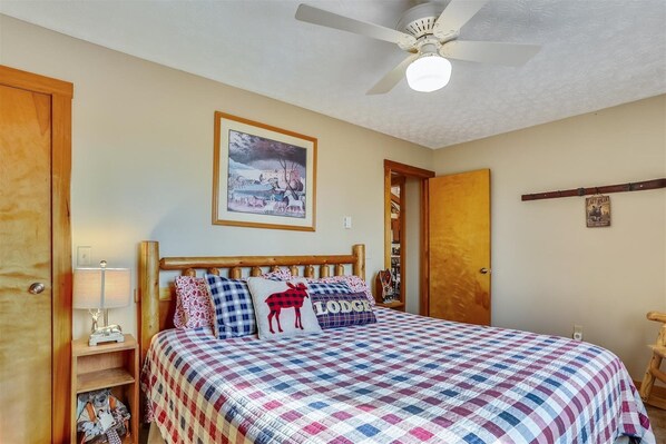 A bedroom with a bed, a ceiling fan, a framed picture on the wall, and a wooden door.