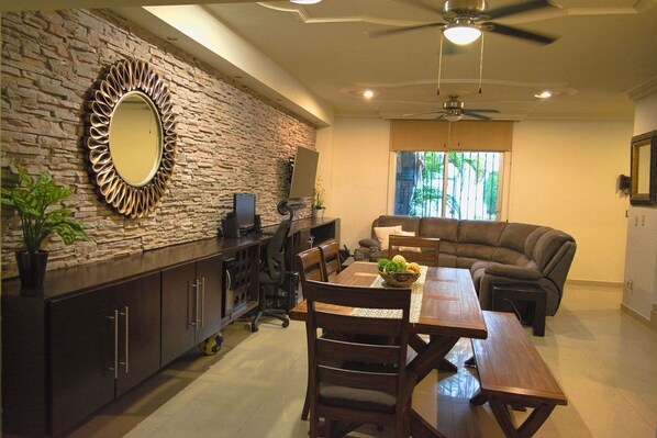 A spacious living area with a stone wall, a large mirror, a dining table, and a comfortable sofa. - Private house, pool, bbq and jacuzzi!! (Mazatlán)
