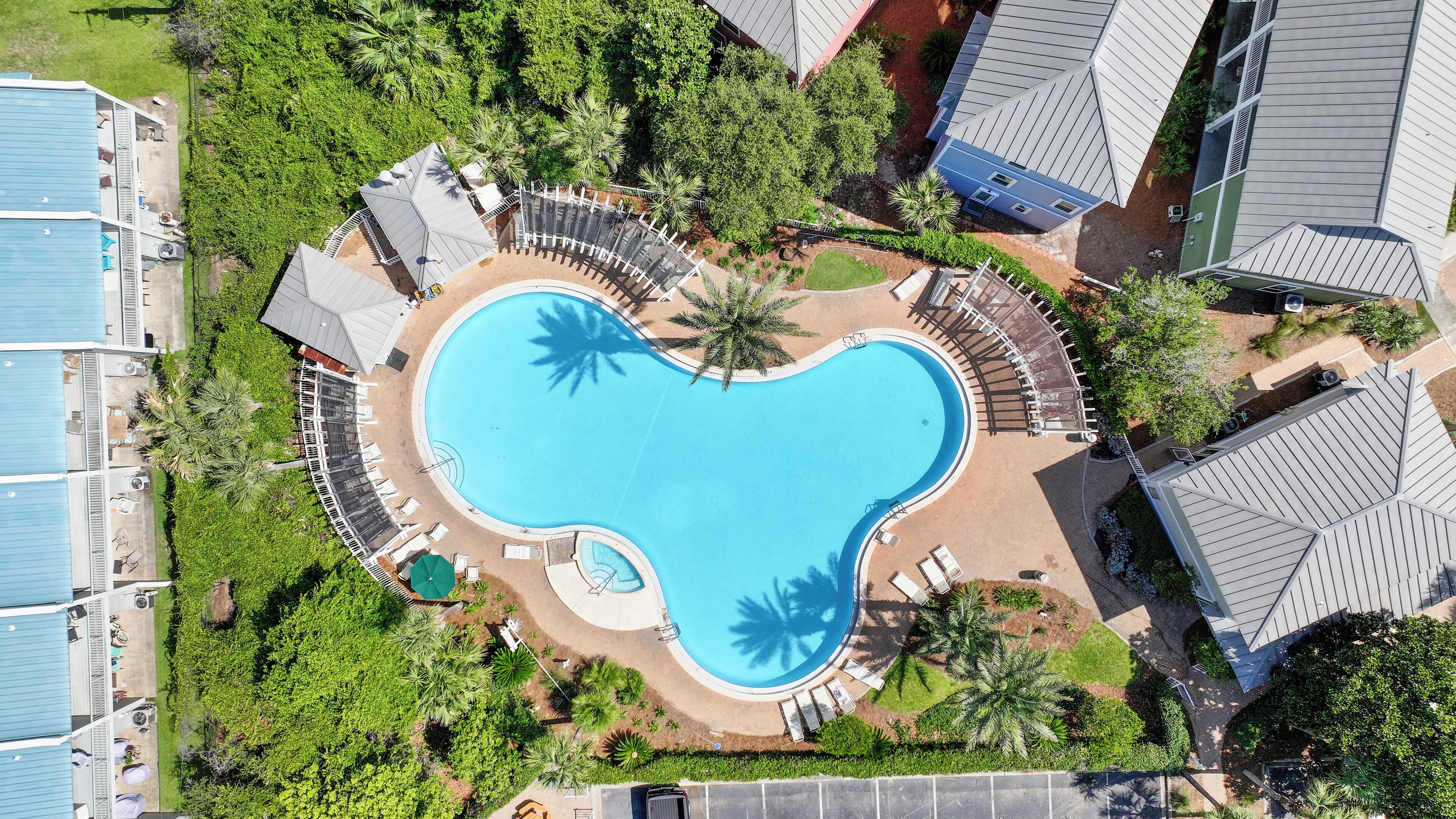 Luchtbeeld van een resort met een zwembad in de vorm van een hart, omgeven door ligbedden en palmbomen.