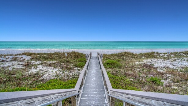A wooden boardwalk leading to a beach with clear turquoise water.
