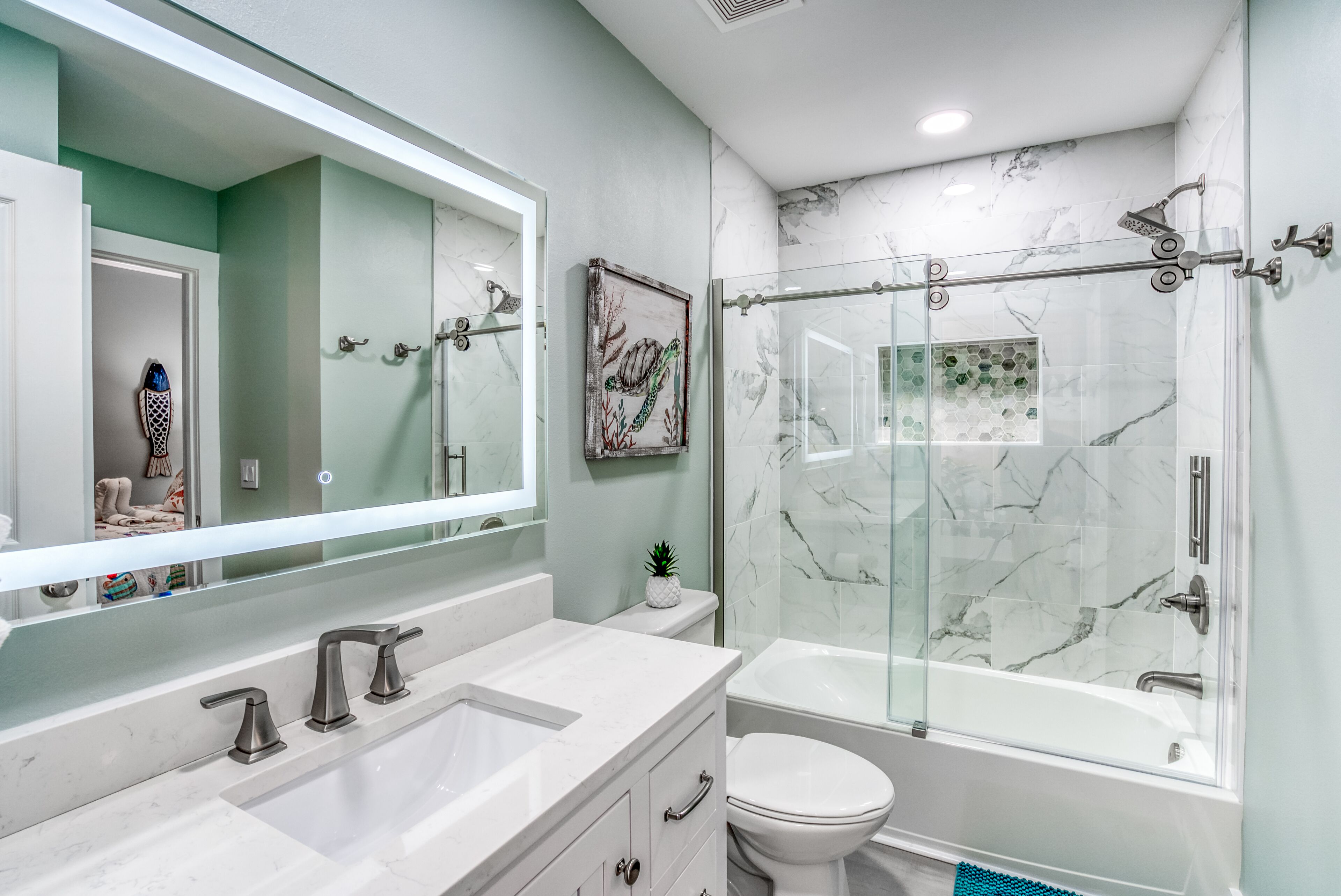 A modern bathroom with a glass-enclosed shower, a white sink with two faucets, a toilet, and a large mirror.