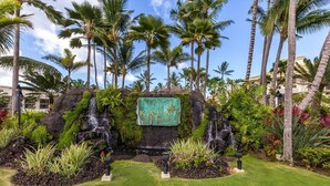 Entree van een tropisch resort met palmbomen, een waterval en een bord waarop staat 
