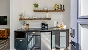Una cocina moderna con armarios oscuros, un microondas integrado, una cafetera y un fregadero. Hay objetos decorativos en los estantes sobre la encimera.