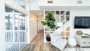 Uma sala de estar moderna com uma televisão grande, um sofá branco e uma escada que dá para uma varanda.