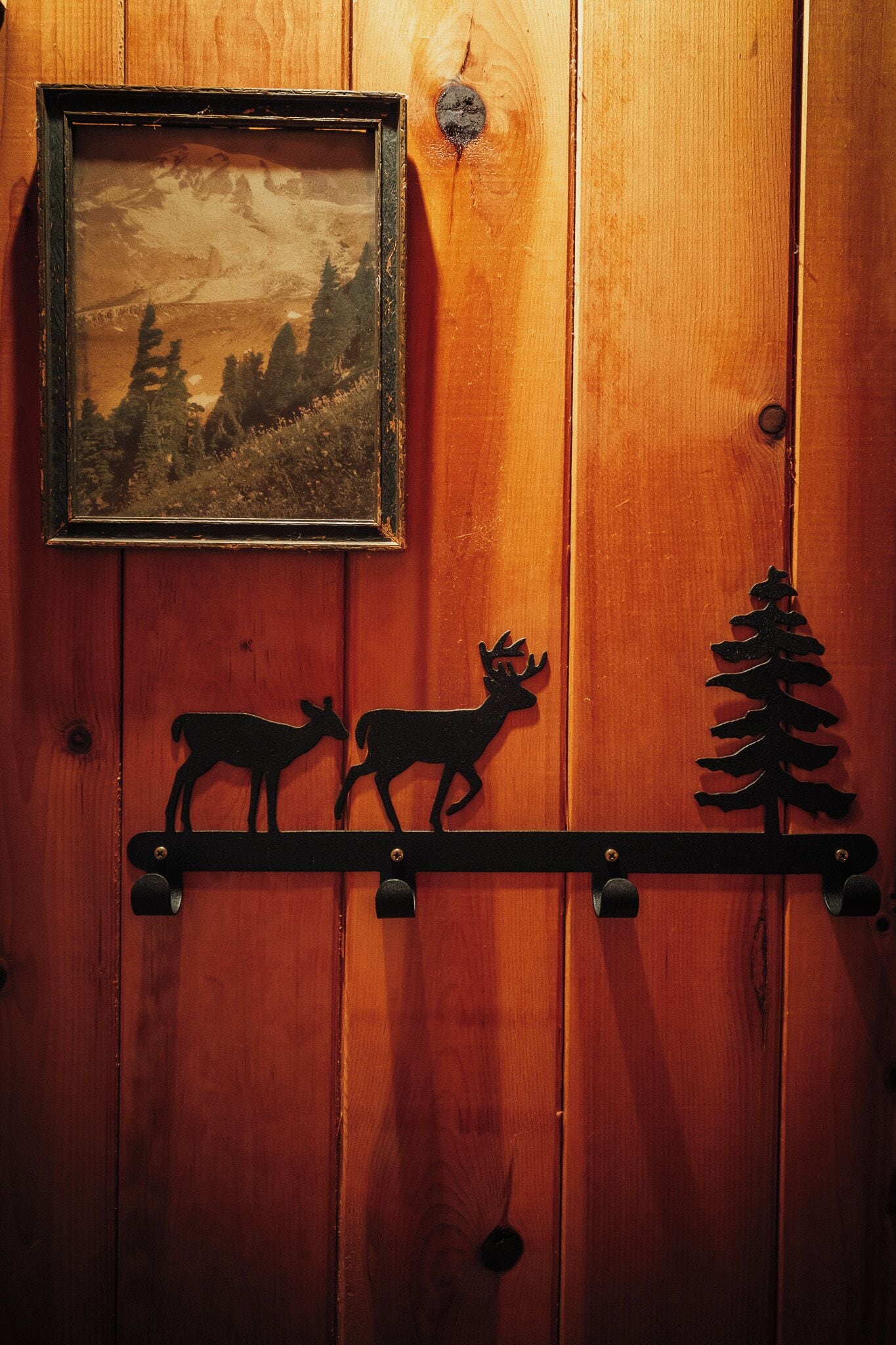Una pared de madera con un cuadro de un paisaje, la silueta de un ciervo y un árbol.