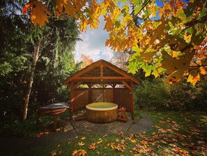 A wooden gazebo with a hot tub, surrounded by autumn foliage.