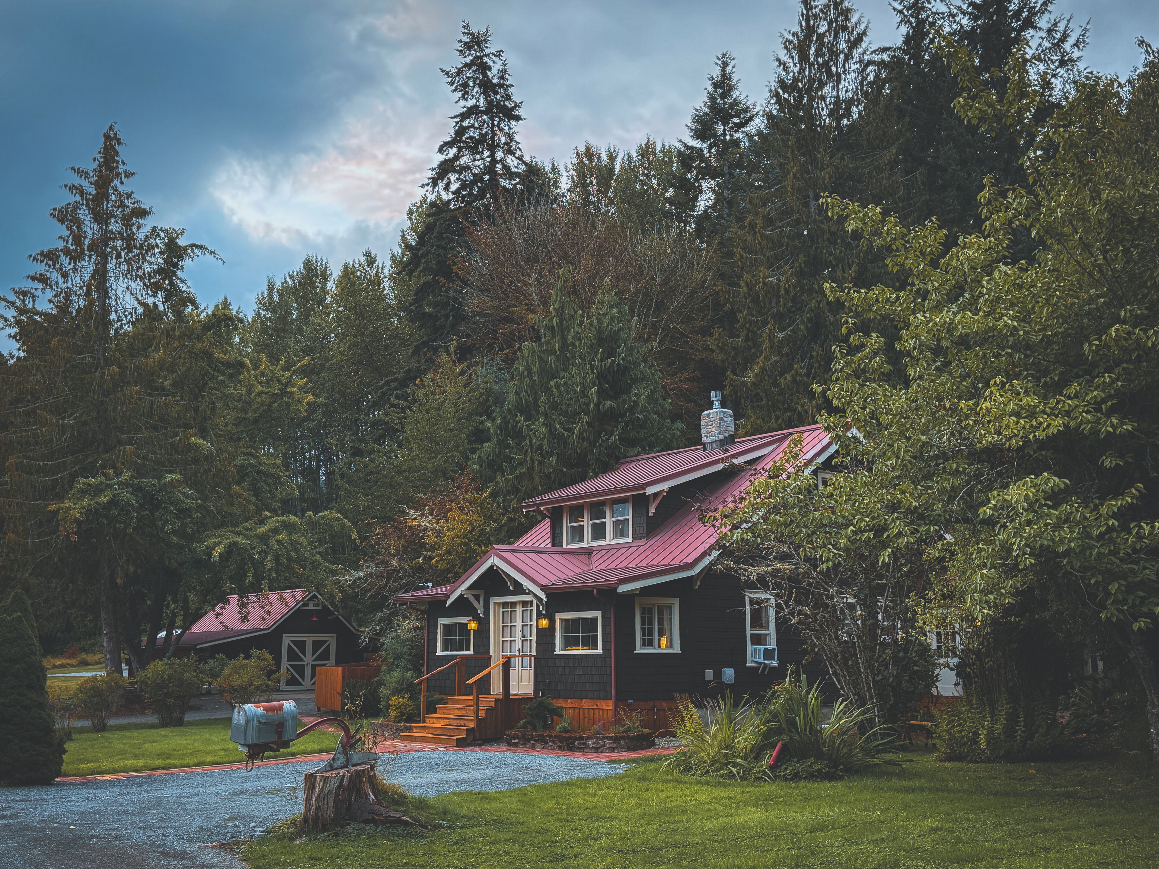 A two-story house with a red roof, surrounded by dense forest.