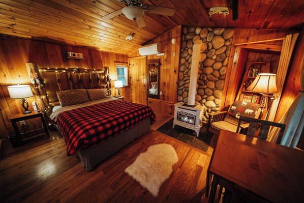 A cozy cabin-style room with a bed, a fireplace, wooden walls, and a stone accent wall.