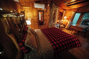 A cozy wooden cabin room with a bed, a stone wall, and a window.
