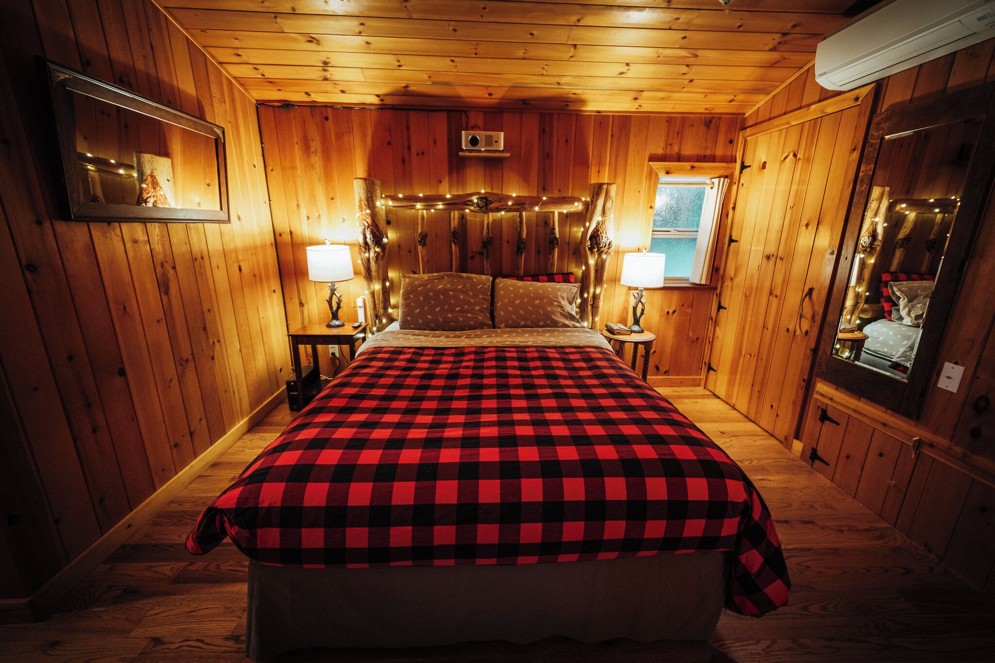 A wooden cabin bedroom with a bed, two bedside lamps, and a mirror.