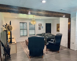 A living room with a fireplace, leather sofas, a chandelier, and a rustic ceiling.