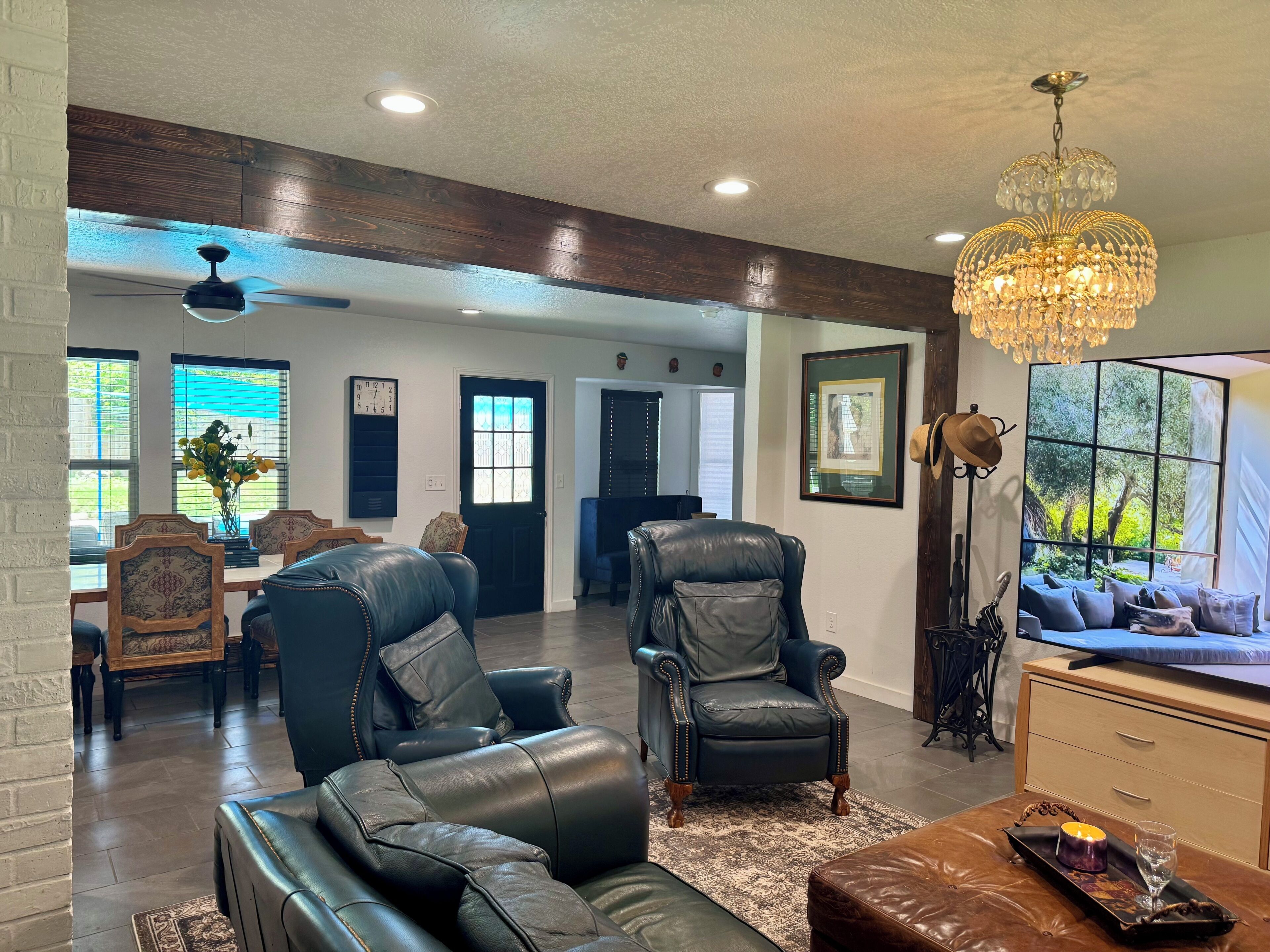 A spacious living room with a fireplace, leather sofas, a chandelier, and a large window with a view.