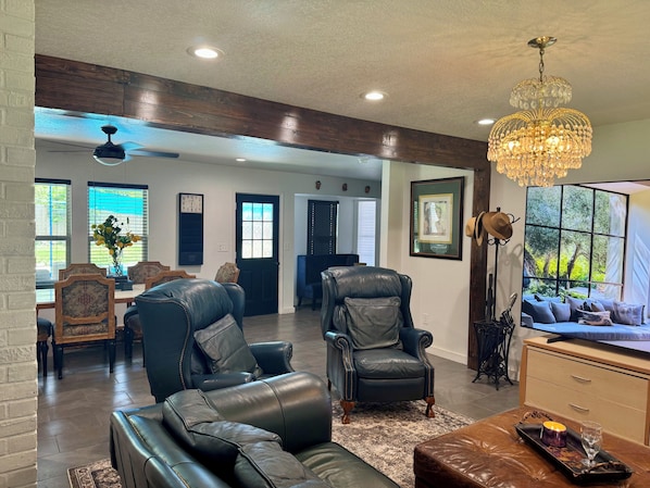 A spacious living room with a fireplace, leather sofas, a chandelier, and a large window with a view.