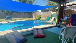 Un jardin avec une piscine, des chaises longues et un espace ombragé.