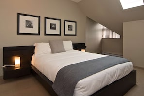 A bedroom with a bed, nightstands, a wall-mounted heater, and three framed pictures.
