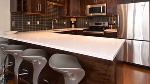 Una cocina moderna con armarios de madera oscura, electrodomésticos de acero inoxidable, una isla grande con taburetes y un salpicadero de azulejos.