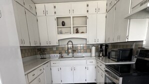 A kitchen with white cabinets, a black stove, a microwave, and a sink. - Beach house sleeps 12 people. Watch the ocean and sunrise at the front patio.  (Carrabelle)