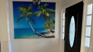 A hallway with a tiled floor, a door with a decorative glass panel, and a wall mural of a beach scene. - Beach house sleeps 12 people. Watch the ocean and sunrise at the front patio.  (Carrabelle)