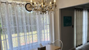 A dining area with a chandelier, a table with chairs, and a clock on the wall. - Beach house sleeps 12 people. Watch the ocean and sunrise at the front patio.  (Carrabelle)