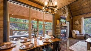 A wooden dining area with a fireplace, large windows, and a stone wall. - Secluded! Game Room! Prkwy & Dollywood around the corner! Private deck! Hot Tub! (Sevierville)