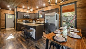 A wooden cabin kitchen with a central island, bar stools, and a dining table set for four. - Secluded! Game Room! Prkwy & Dollywood around the corner! Private deck! Hot Tub! (Sevierville)
