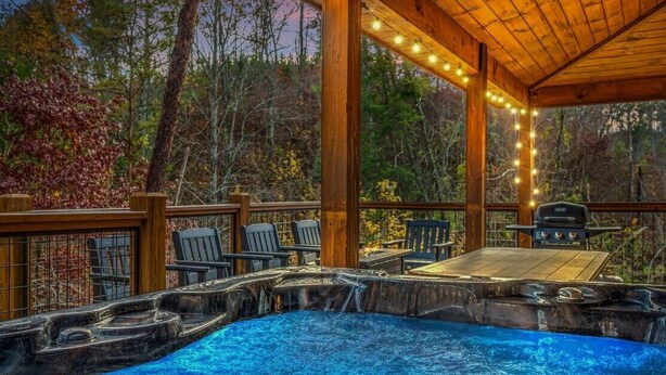 A hot tub with a wooden deck, surrounded by chairs and a grill. - Secluded! Game Room! Prkwy & Dollywood around the corner! Private deck! Hot Tub! (Sevierville)