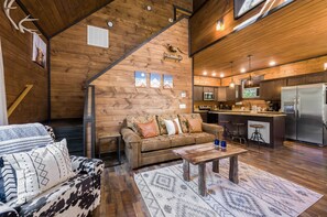 L’intérieur chaleureux d’un chalet, avec un revêtement mural en bois, un canapé, une table basse et un coin cuisine équipé d’un réfrigérateur et d’un four à micro-ondes.