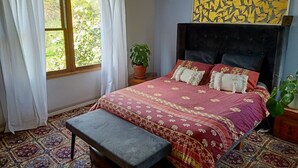 A bedroom with a large bed, a bench, a potted plant, and a window with curtains. - Beautiful Homestead on Two private acres (Drysdale)