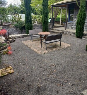 A gravel patio with a bench and table, surrounded by stone walls and greenery. - Beautiful Homestead on Two private acres (Drysdale)