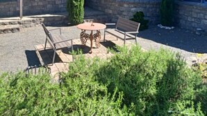 A stone building with a metal roof, a small patio with a table and benches, and a large tree in the foreground. - Beautiful Homestead on Two private acres (Drysdale)