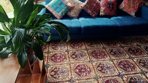 A blue sofa with patterned cushions, a large green plant, and a detailed rug. - Beautiful Homestead on Two private acres (Drysdale)