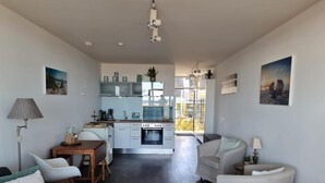 A modern living room with a sofa, a dining table, and a kitchen area with cabinets and a stove. - Front row, more sea is not possible! (Haffkrug)