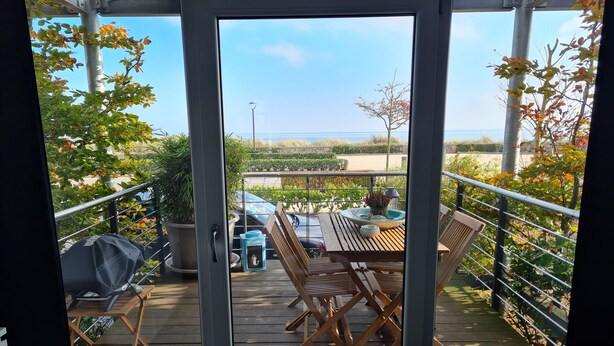 A balcony with a wooden table and chairs, a barbecue grill, and potted plants. - Front row, more sea is not possible! (Haffkrug)
