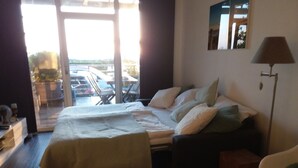 A hotel room with a bed, a chair, a desk, and a view of the outside. - Front row, more sea is not possible! (Haffkrug)