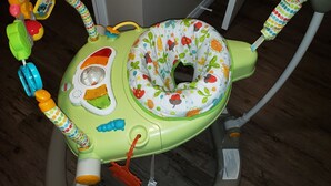 Ein Babywippstuhl mit einem Sitzkissen in farbigem Blattmuster, ein Spielzeug mit einem gelben Griff und ein blaues Raupen-Spielzeug.