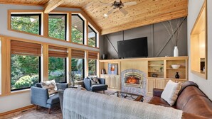 A spacious living room with a fireplace, large windows, and a television.