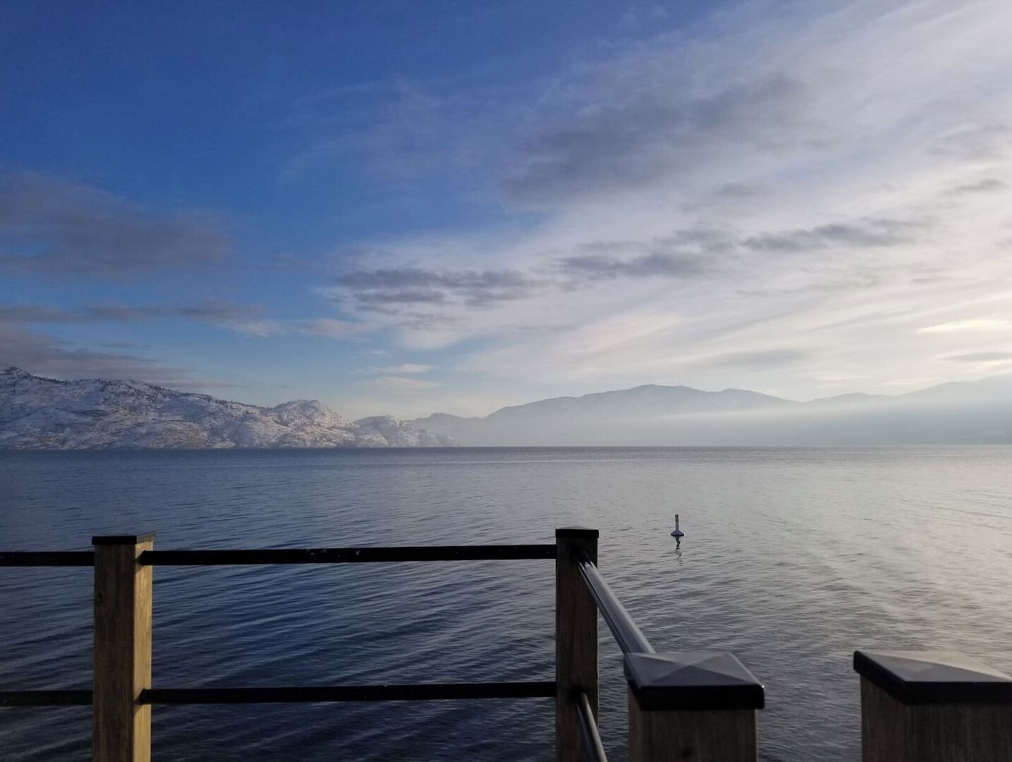 A calm lake with mountains in the background and a wooden railing in the foreground.