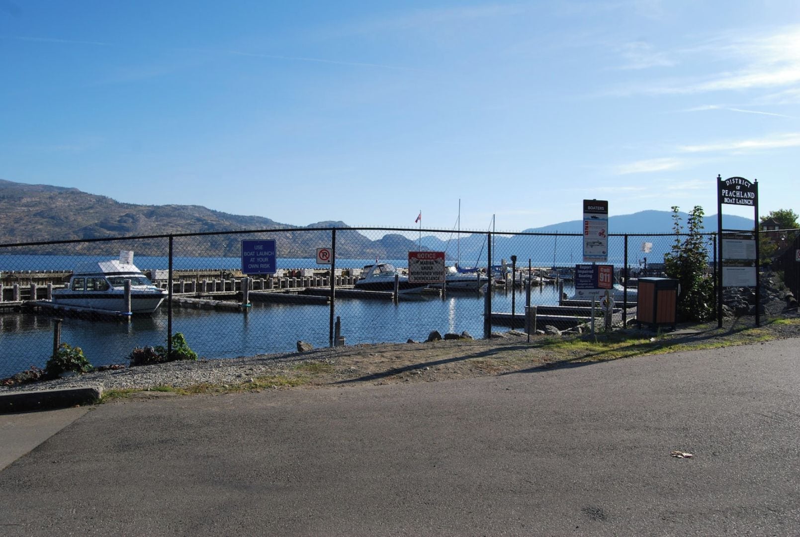A boat launch area with a clear view of the water and boats, a sign indicating a 911 emergency call point, and a notice about boat launch safety.