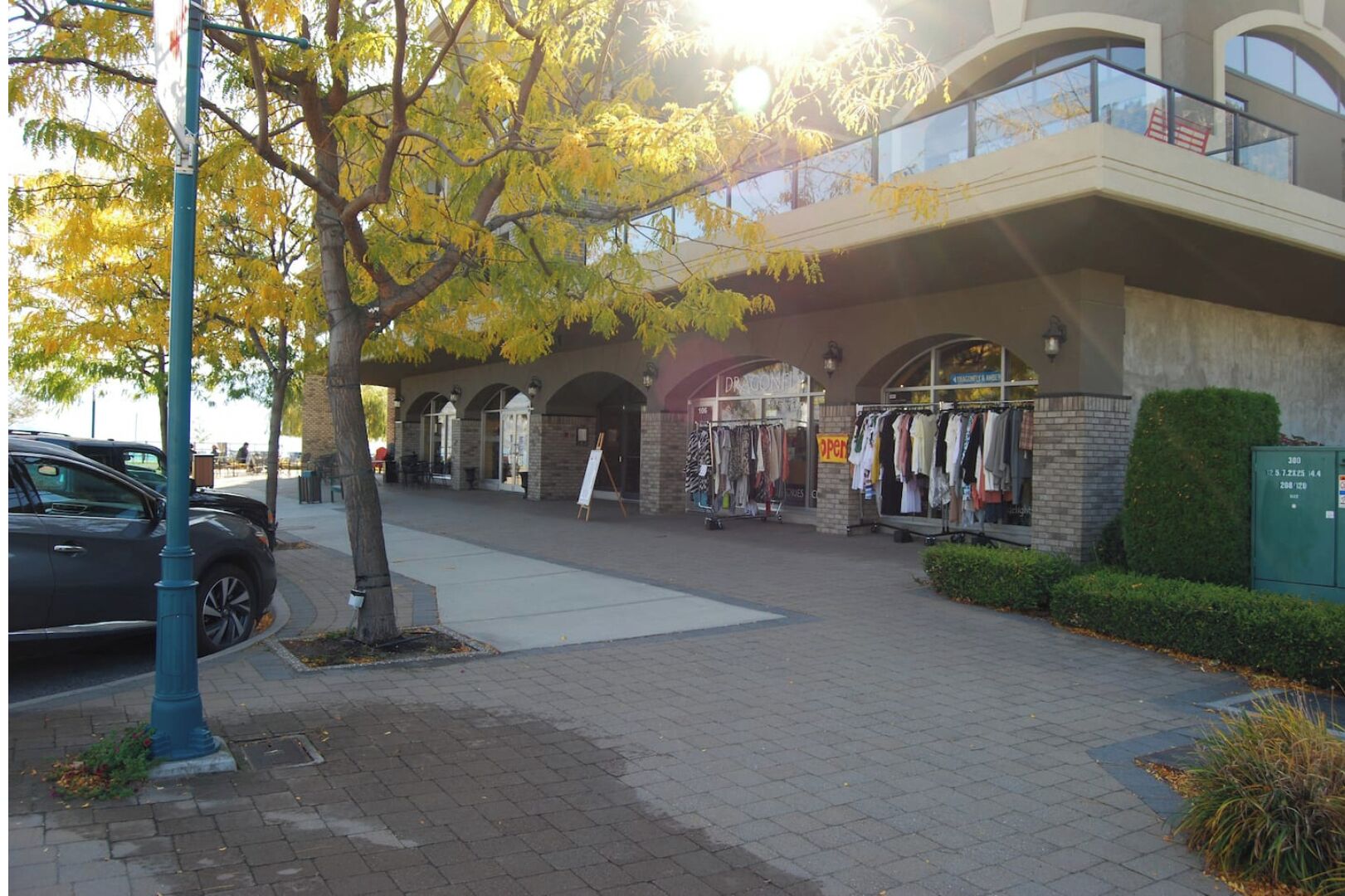 A shopping area with a brick pathway, a tree, and a building with a storefront.