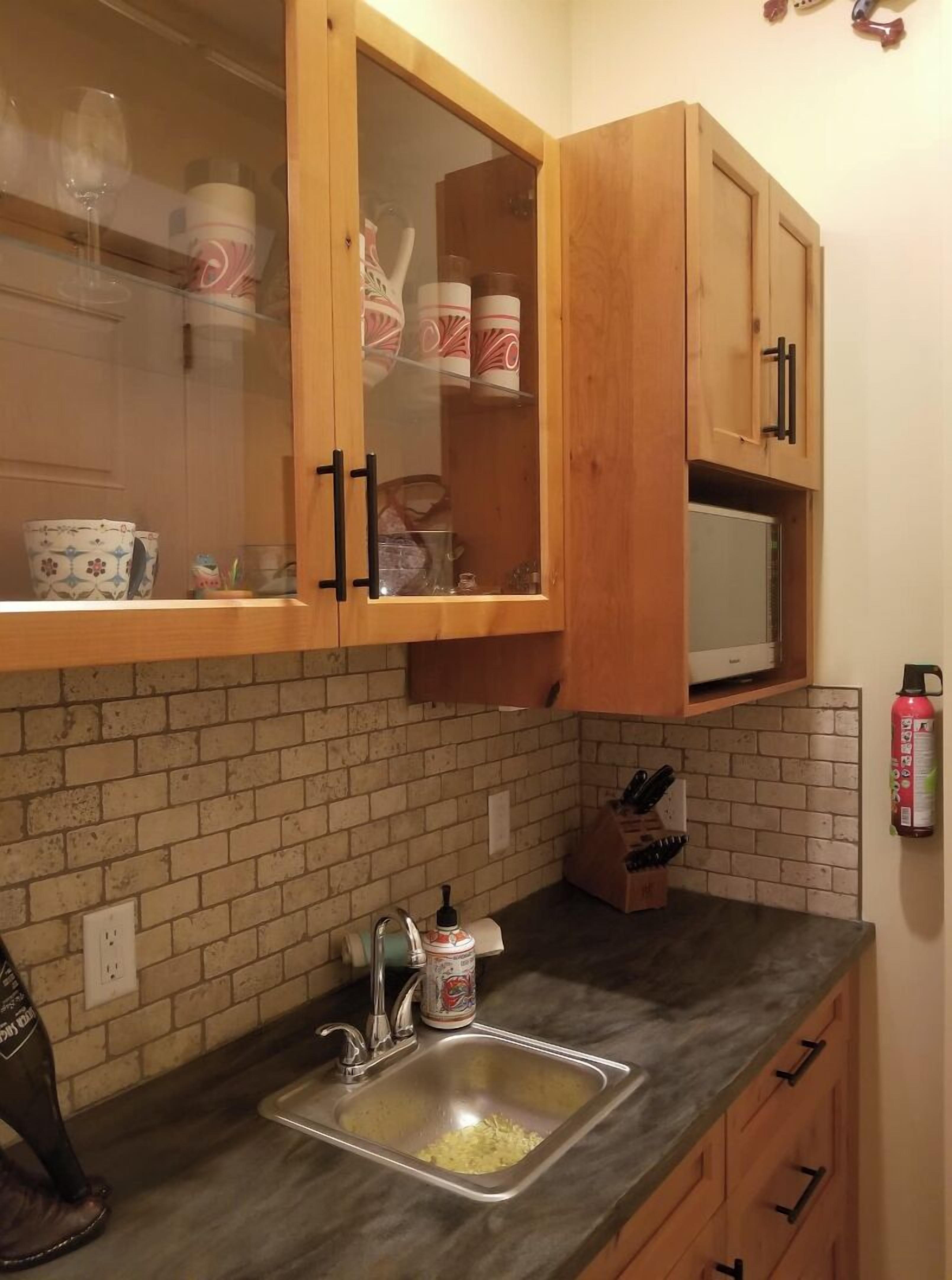 A kitchen with wooden cabinets, a brick backsplash, a stainless steel sink, and a microwave.